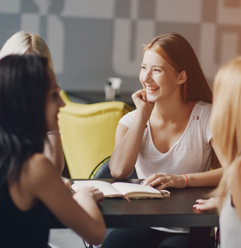 four young beautiful girls sitting in a cafe talking and doing business affairs